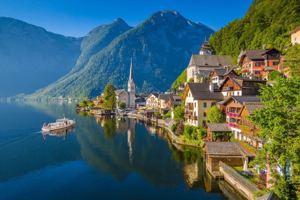 Scenic picture-postcard view of famous Hallstatt lakeside town in the Austrian Alps with passenger ship in beautiful morning light at sunrise on a sunny day in summer, Salzkammergut region, Austria