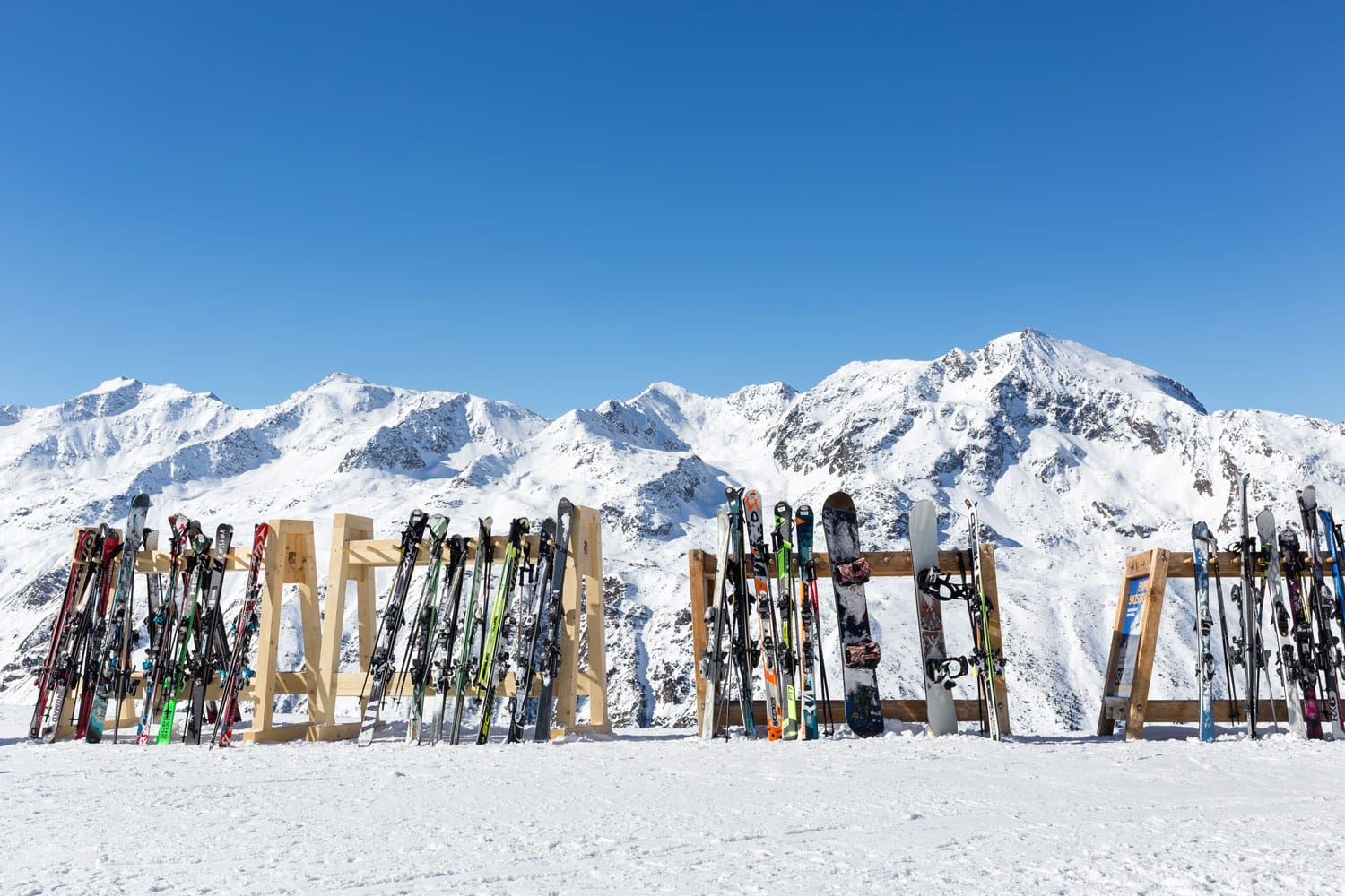 A line of skis and snowboards stored on racks outside a cafe on the slopes at Hochgurgl with the Otztal Alps in the background.