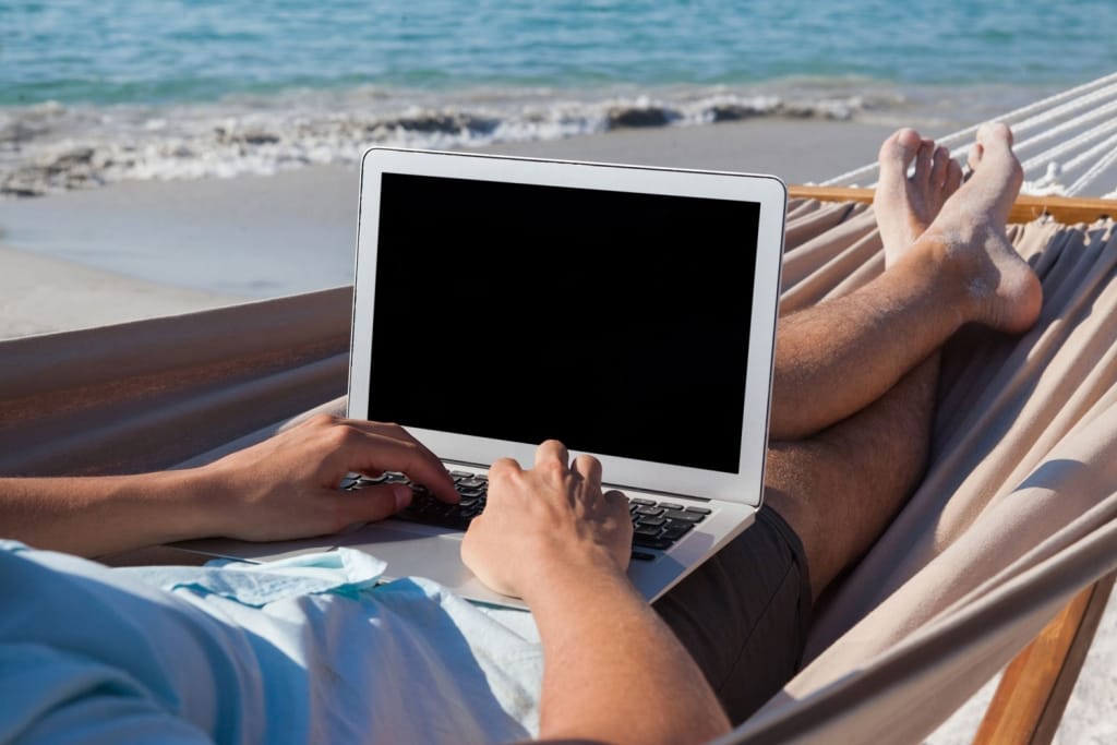 Man using laptop while relaxing on hammock in beach