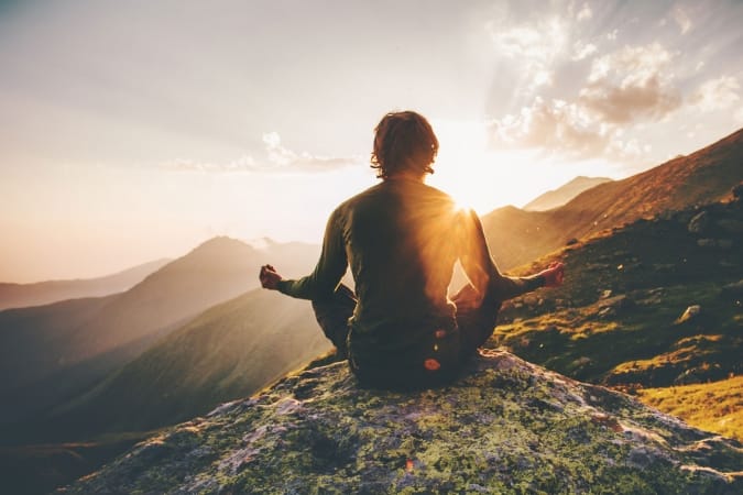 Man meditating on top of a mountains