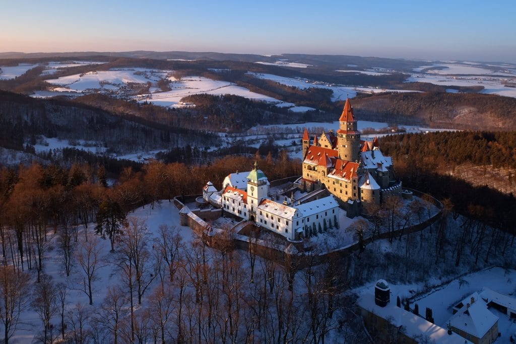 Aerial view on romantic fairy castle in winter picturesque winter landscape illuminated by the setting sun. Gothic castle in winter highland surrounded by trees. Bouzov castle, Czech republic.