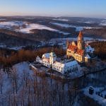 Aerial view on romantic fairy castle in winter picturesque winter landscape illuminated by the setting sun. Gothic castle in winter highland surrounded by trees. Bouzov castle, Czech republic.