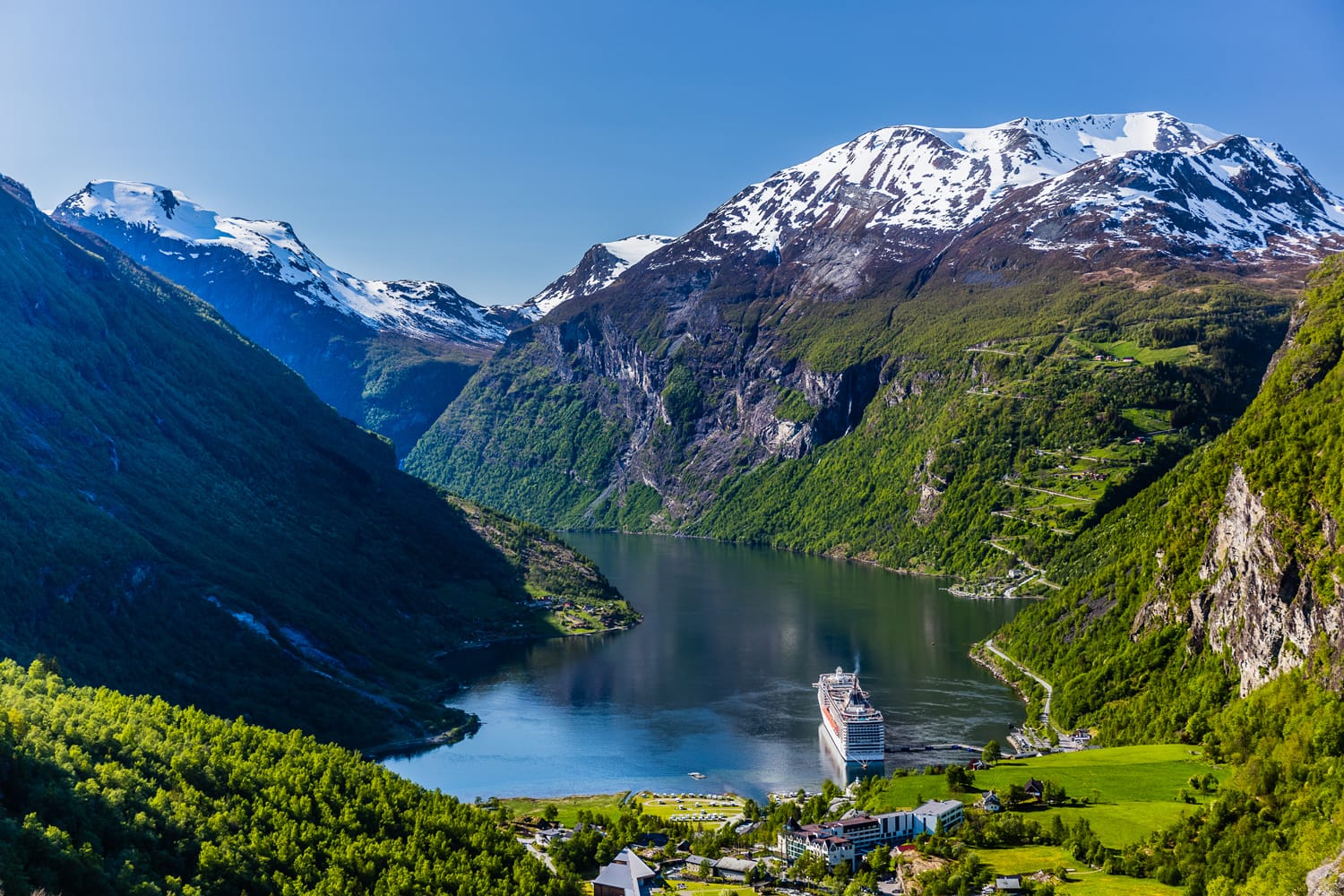 Geirangerfjord with a ship in a port from above, with mountain peaks covered with snow