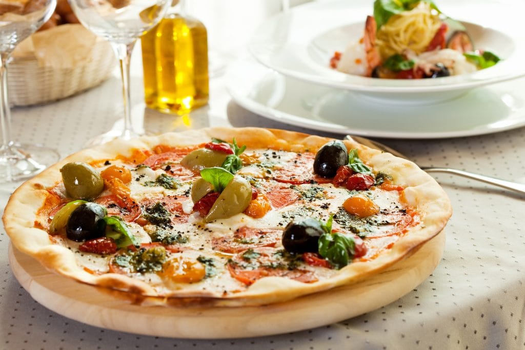 Pizza with Mozzarella Cheese, Fresh Tomato and Pesto Sauce. Served at Restaurant Table