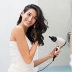 Beautiful girl using a hair dryer and smiling while looking at the mirror. Smiling woman drying hair with hair dry machine.