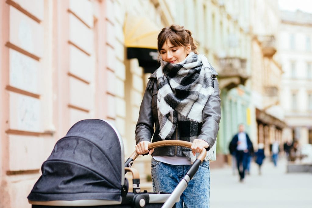 Young beautiful mother walking with baby carriage in european city center.