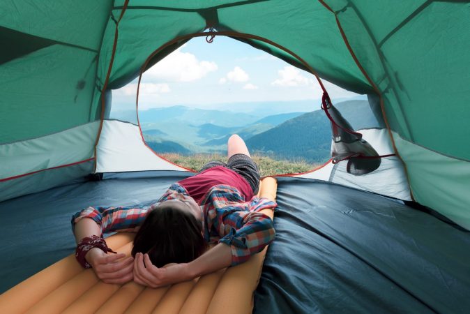 Girl lies in they tent against the backdrop of an incredible mountain landscape