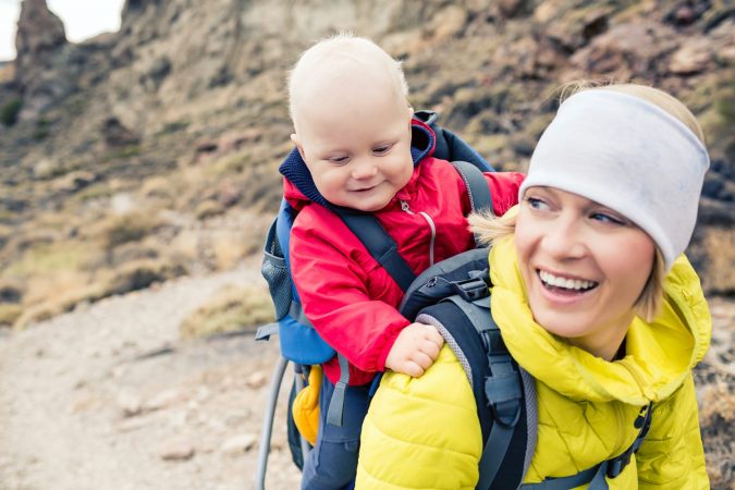 Happy mother with little boy travelling in backpack