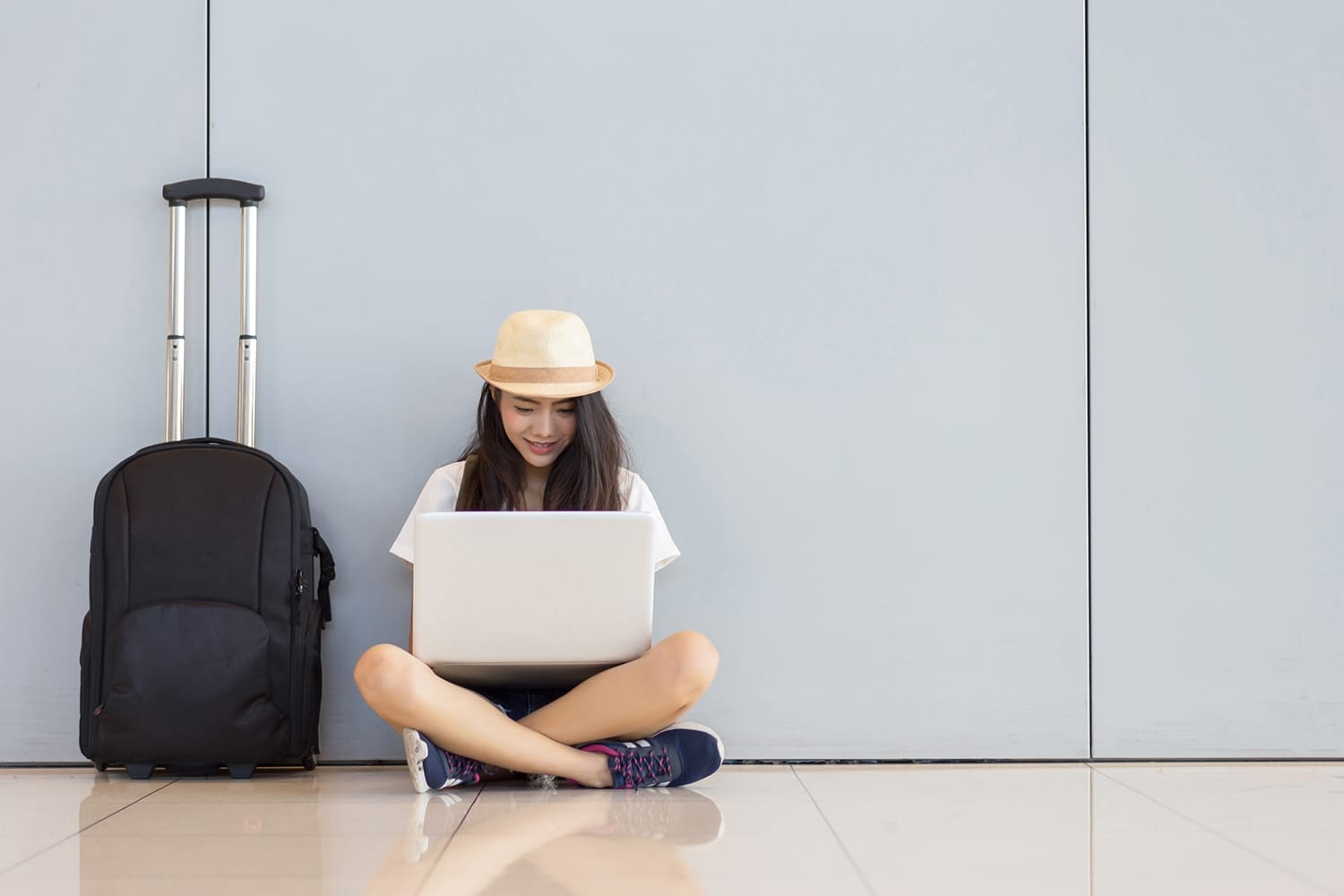 Gadis remaja asia menggunakan laptop di terminal bandara duduk dengan koper bagasi dan ransel untuk perjalanan liburan musim panas dengan santai menunggu transportasi penerbangan atau pemesanan tiket