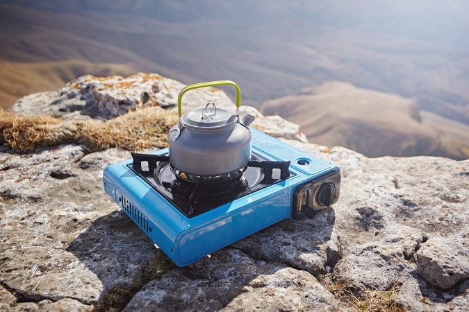 Portable camping gas stove with a gray kettle on a background of nature in the mountains.