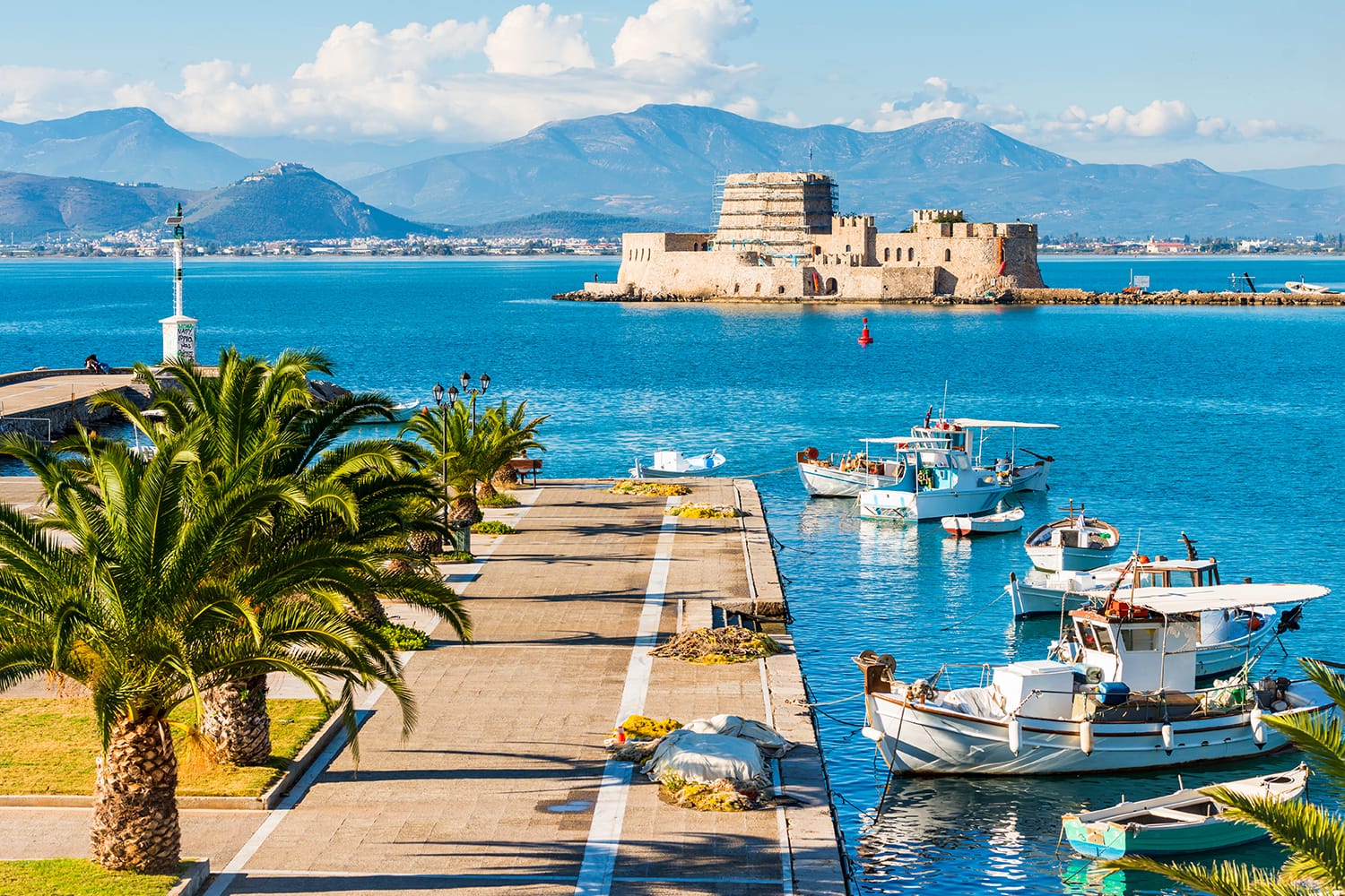 Beautiful port of Nafplio city in Greece with small boats, palm trees and Bourtzi castle on the water