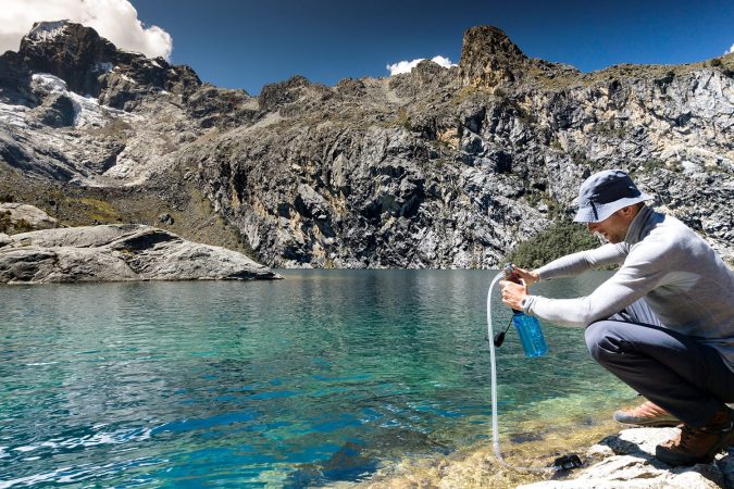 oung mountain climber filtering and pumping water for drinking from a turquoise mountain lake high up in the Peruvian Andes