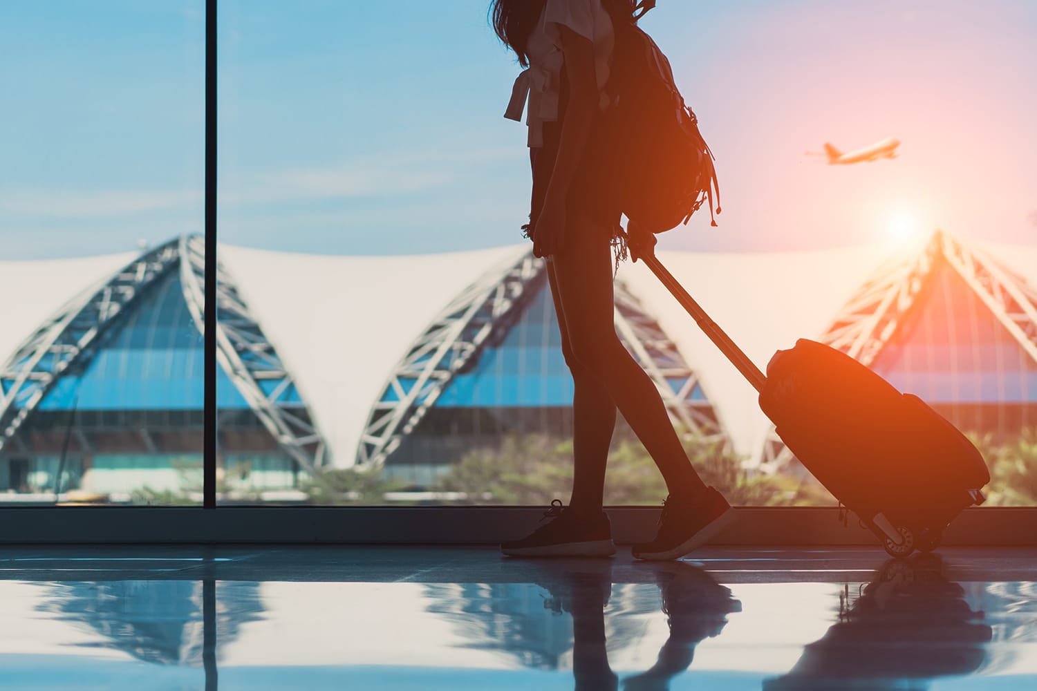 Siluet pelancong wanita dengan barang bawaan berjalan melalui jendela samping di terminal bandara internasional atau gadis remaja bepergian pada liburan musim panas bersantai dengan koper dan ransel