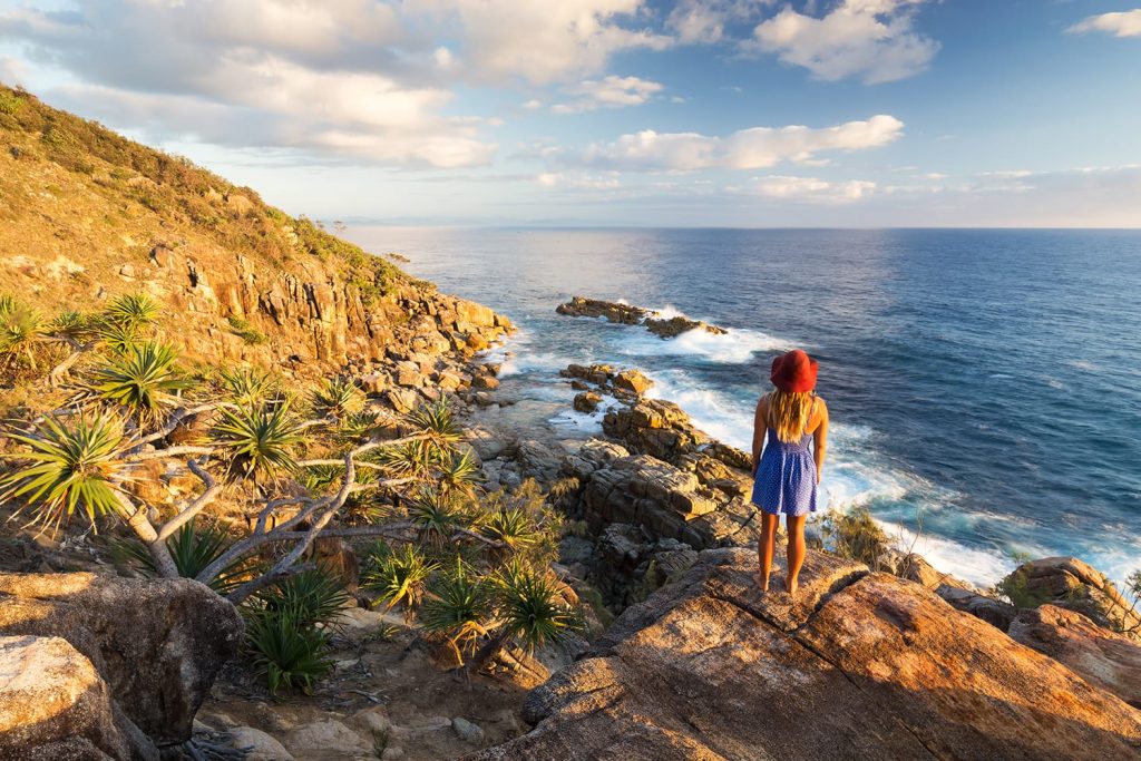 A young woman admires a coastal view at sunrise near Coffs Harbour, Australia.