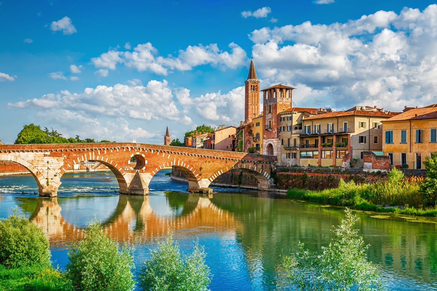 Panoramic view to Bridge Ponte Pietra in Verona on Adige river. Veneto region. Italy. Sunny summer day panorama and blue dramatic sky with clouds. Ancient european italian terracotta color houses