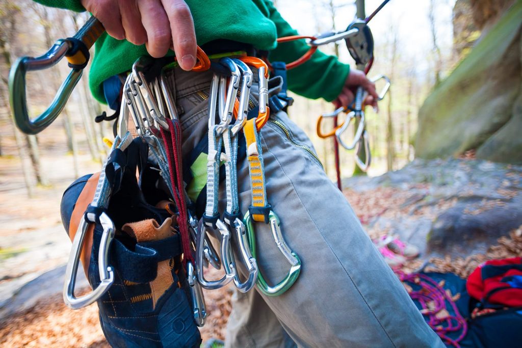 Climber partner insures. Quickdraw, carabiner, and climbing shoes hanging on a safety system