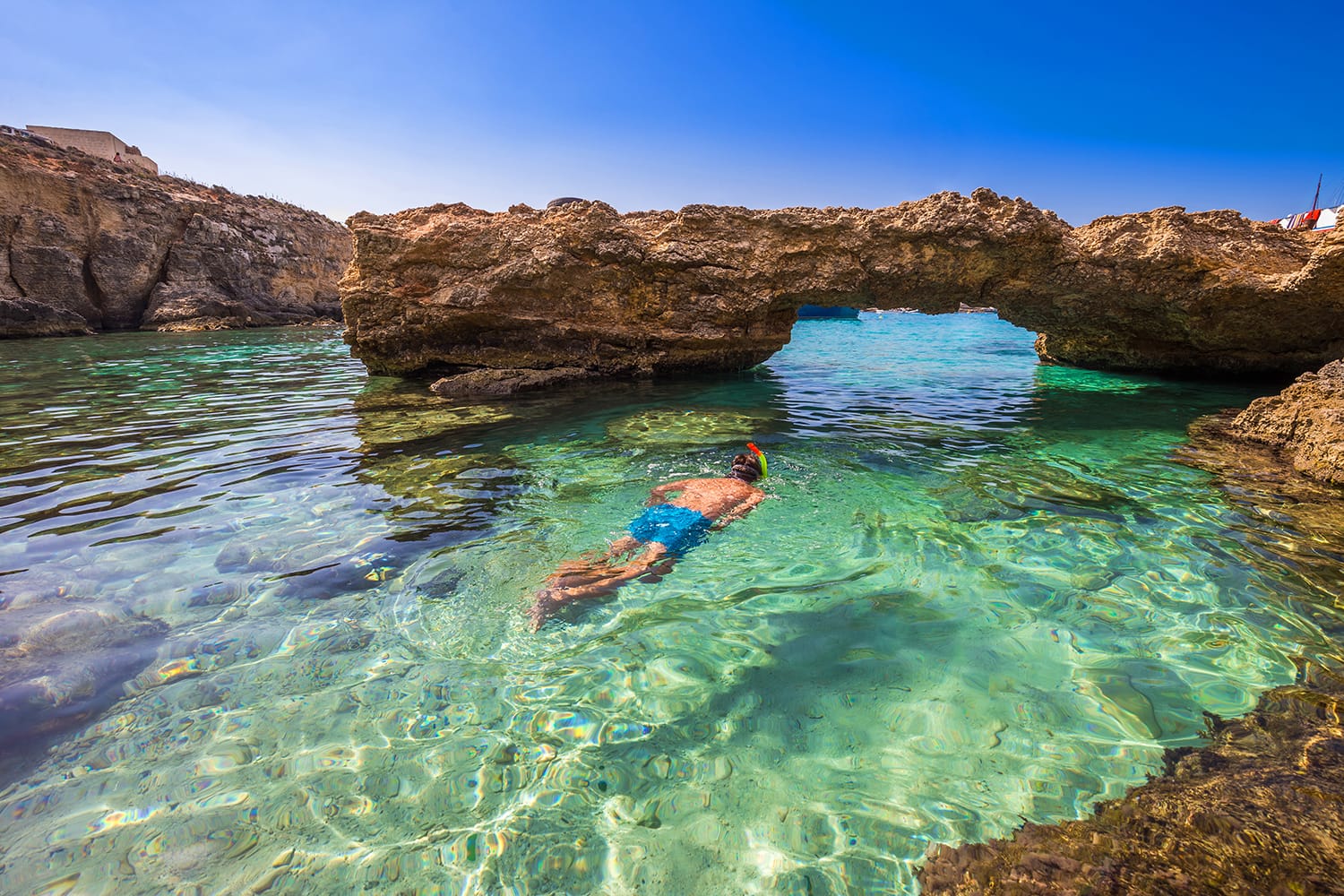 Snorkeling tourist at the caves of the Blue Lagoon on the island of Comino on a bright sunny summer day with blue sky