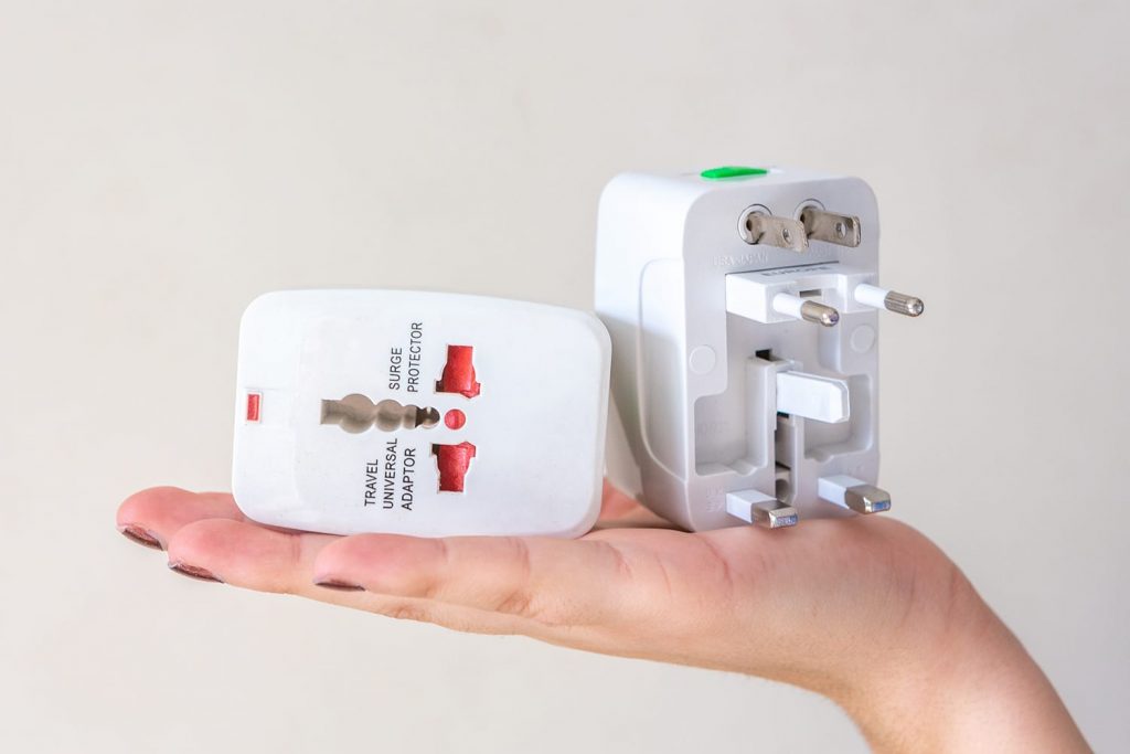 Close up of woman hand holding universal electric socket plug adapters, isolated on white background. Used to connect electrical outlets worldwide