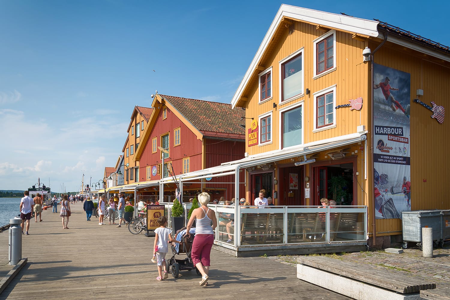 Orang-orang menikmati matahari musim panas di samping restoran alfresco dan gedung apartemen modern di kota Tonsberg, Norwegia