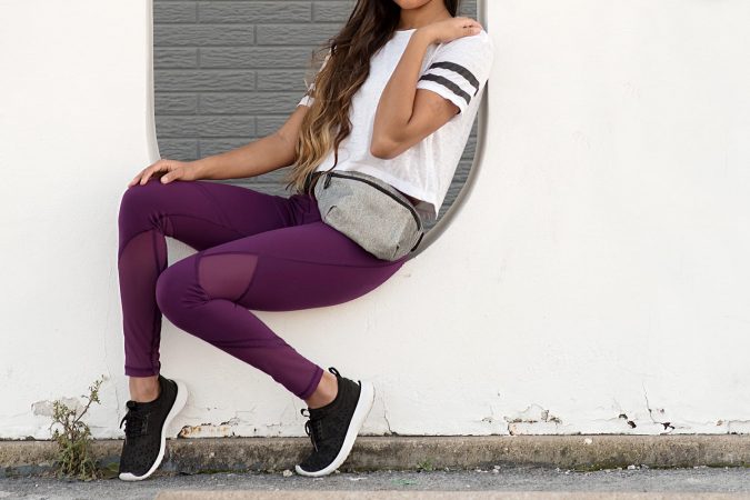 Young Woman Sitting on a White Wall in Sportswear and a Fanny Pack