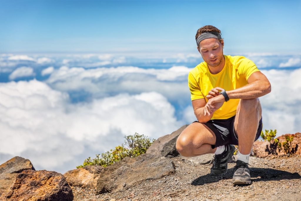 Sport man touching smartwatch on mountain hike trail running summer outdoors sports lifestyle. Athlete fitness runner getting ready to run in mountains.