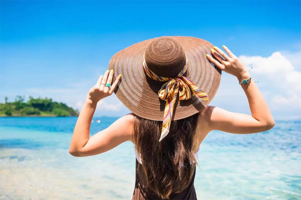 Woman in summer vacation wearing straw hat and beach dress enjoying the view at the ocean
