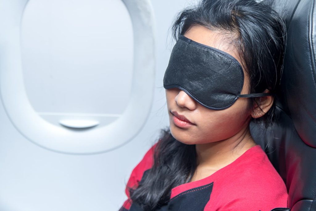Portrait of a woman sleeping in an airplane. Young woman sleeping with a sleep mask on the eyes in a flying aircraft. Girl sleeps in the airplane in a vertical position on seat covered with eye flap.