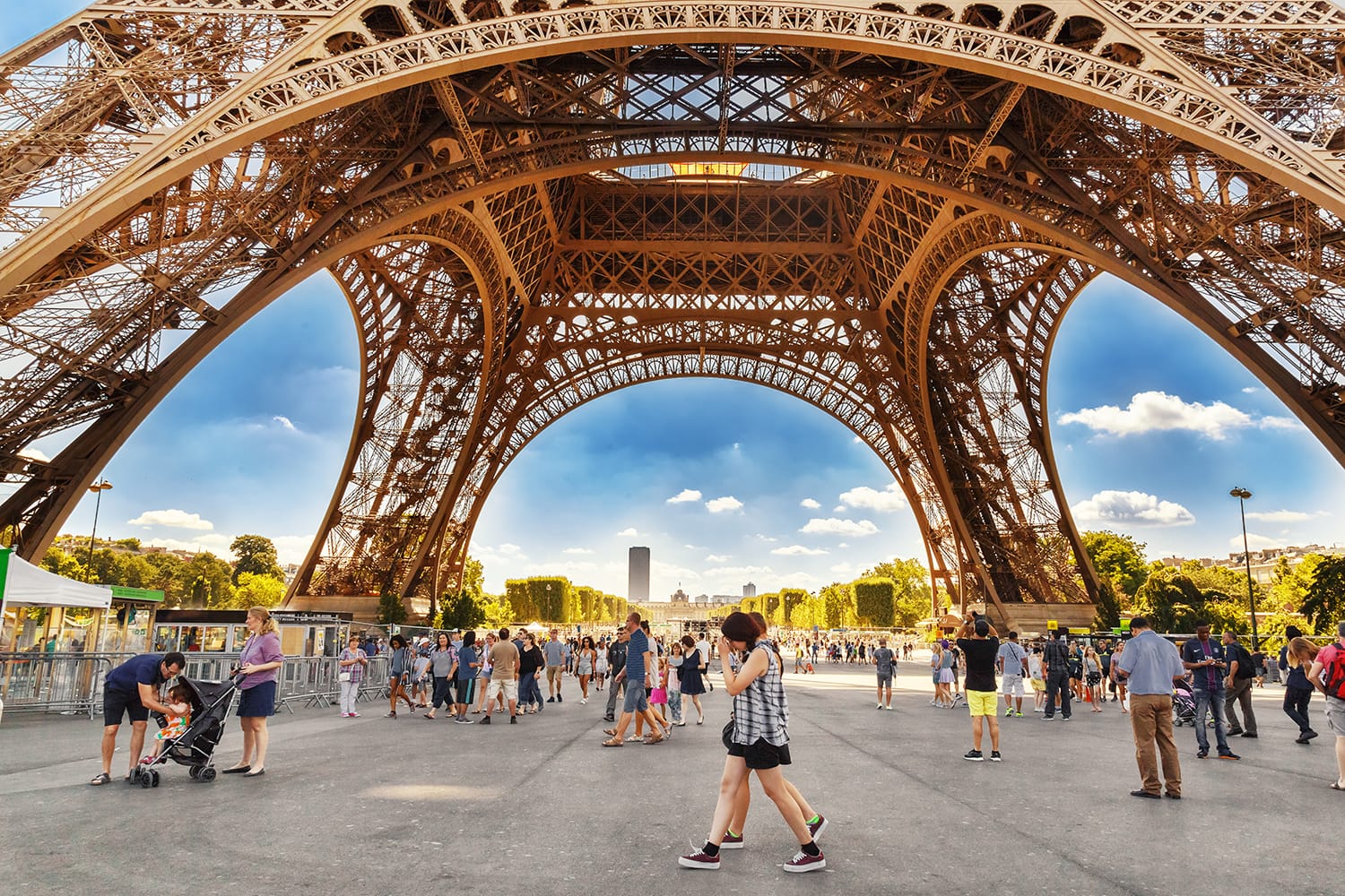 Tourists walking under Eiffel tower (Eiffel tour) in sunny summer day in Paris