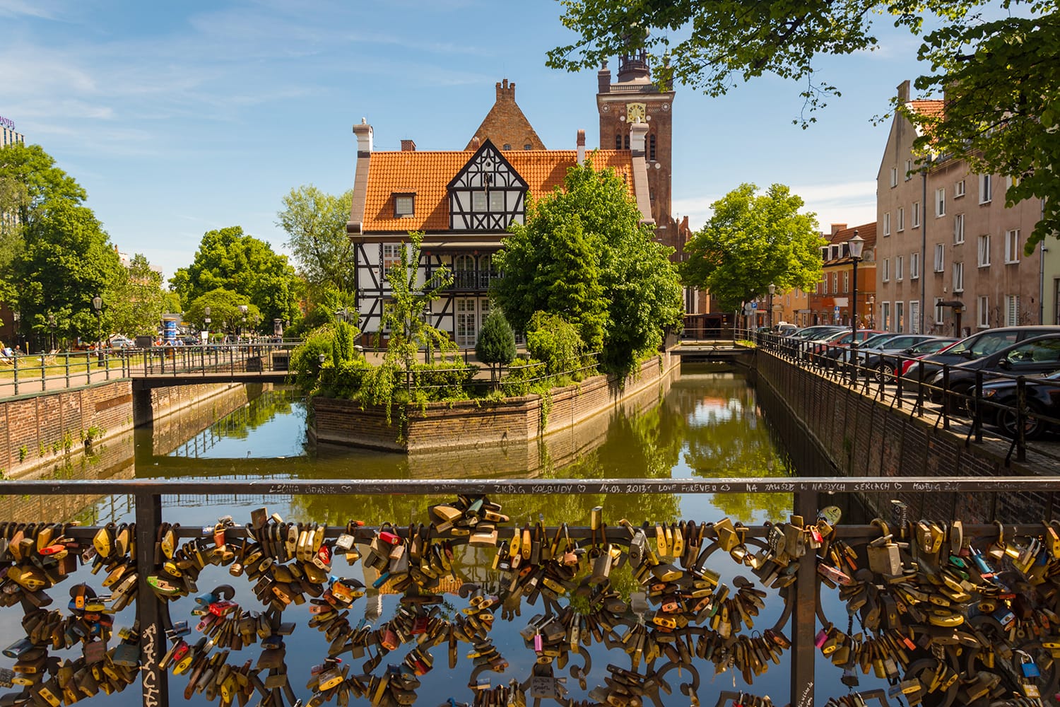 Scenic view on half-timbered building on the river island in european city, church tower on background and padlocks on bridge of love on foreground. Miller house, Grand Mill, Old Town, Gdansk, Poland.