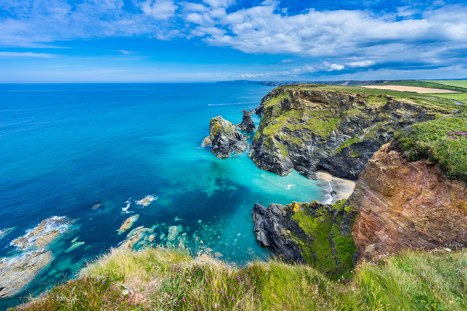 View of the South Devon coast, England, in the summer with clear waters, blue sky and grass.