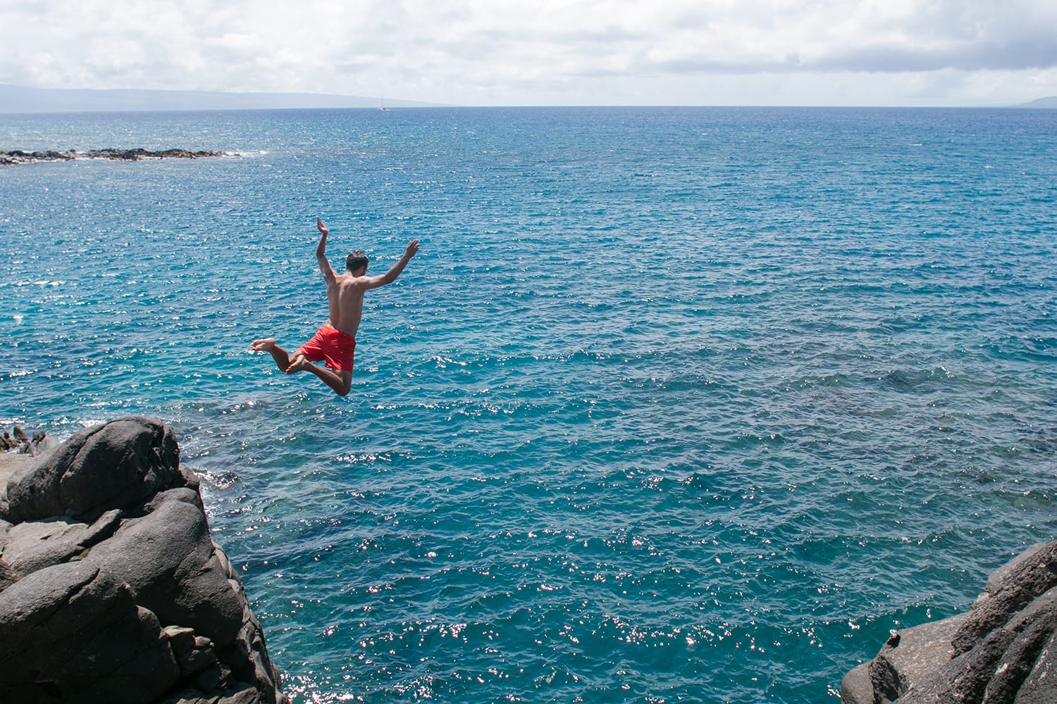 A man jumps off a cliff into the blue ocean in Maui, Hawaii