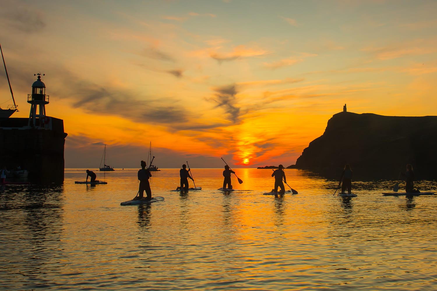 Silhouetted people paddle boarding in Port Erin Bay in the Isle of Man