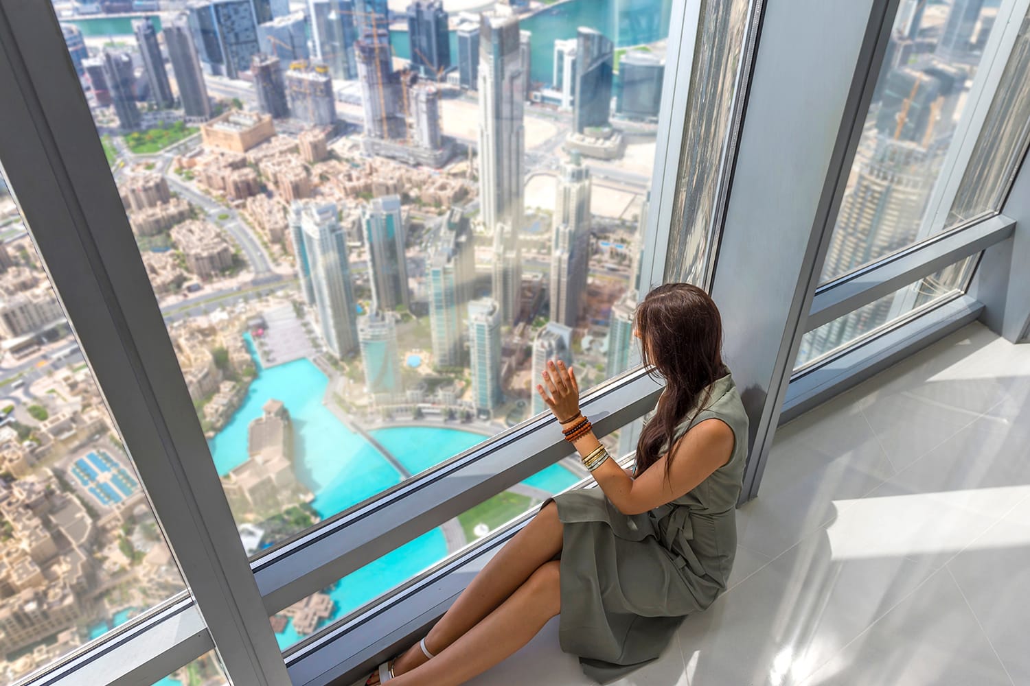 A woman sitting by the window with a panoramic view over the Dubai city and fountains