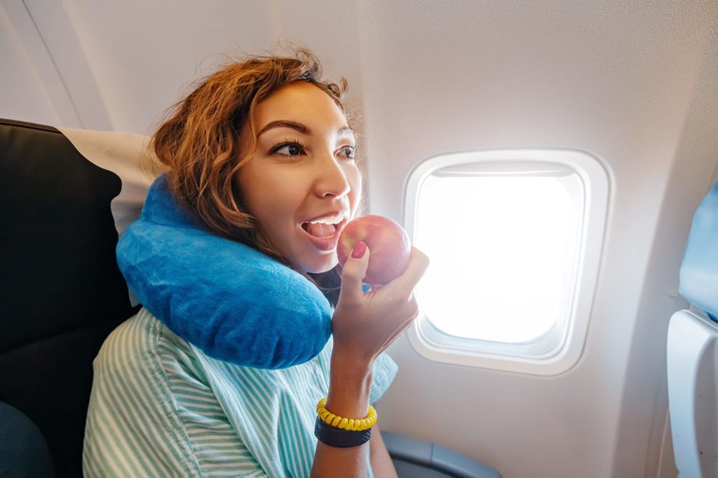 A woman eats a healthy fruit snack in the cabin of an airplane - a ripe red apple