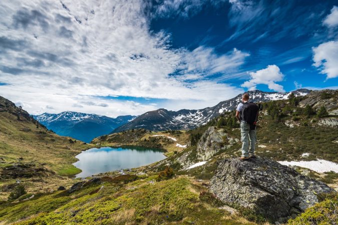 Active hiker with backpack in Pyrenees overlooking lake Tristaina in Andorra