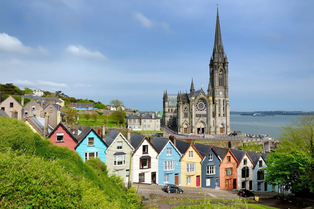 Colorful row houses with towering St. Colman's Cathedral in background in the port town of Cobh, County Cork, Ireland