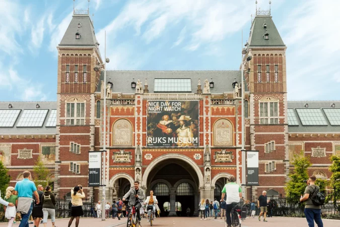 Rijksmuseum building facade with tourists and cyclists on bright summer day in Amsterdam, Netherlands