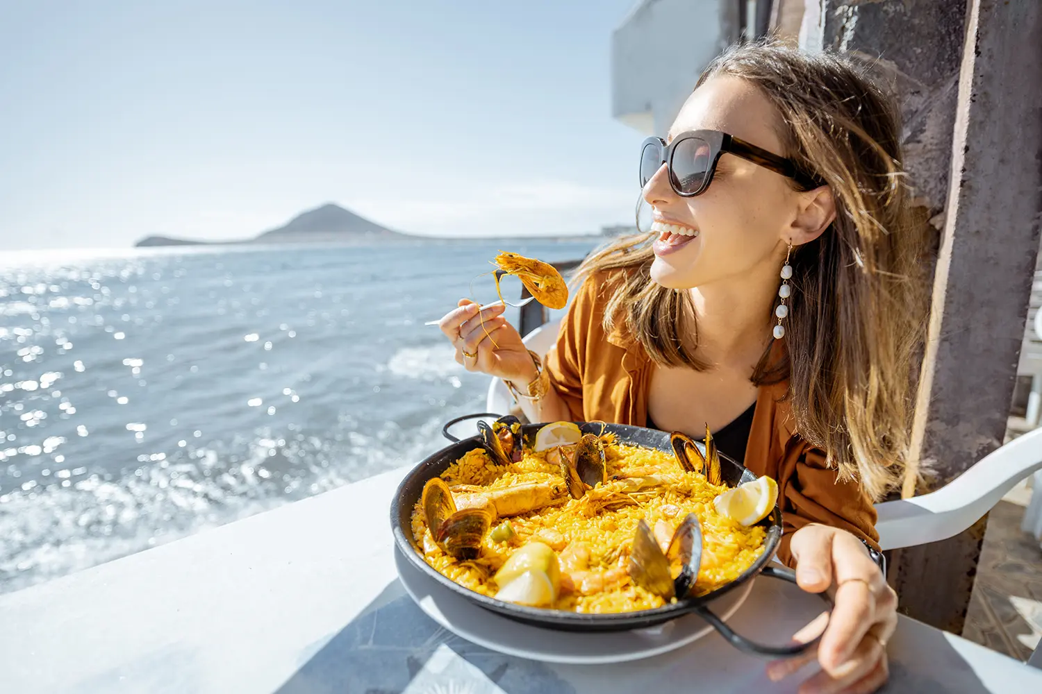 Woman eating paella, traditional spanish dish, while sitting at the restaurant terrace near the ocean