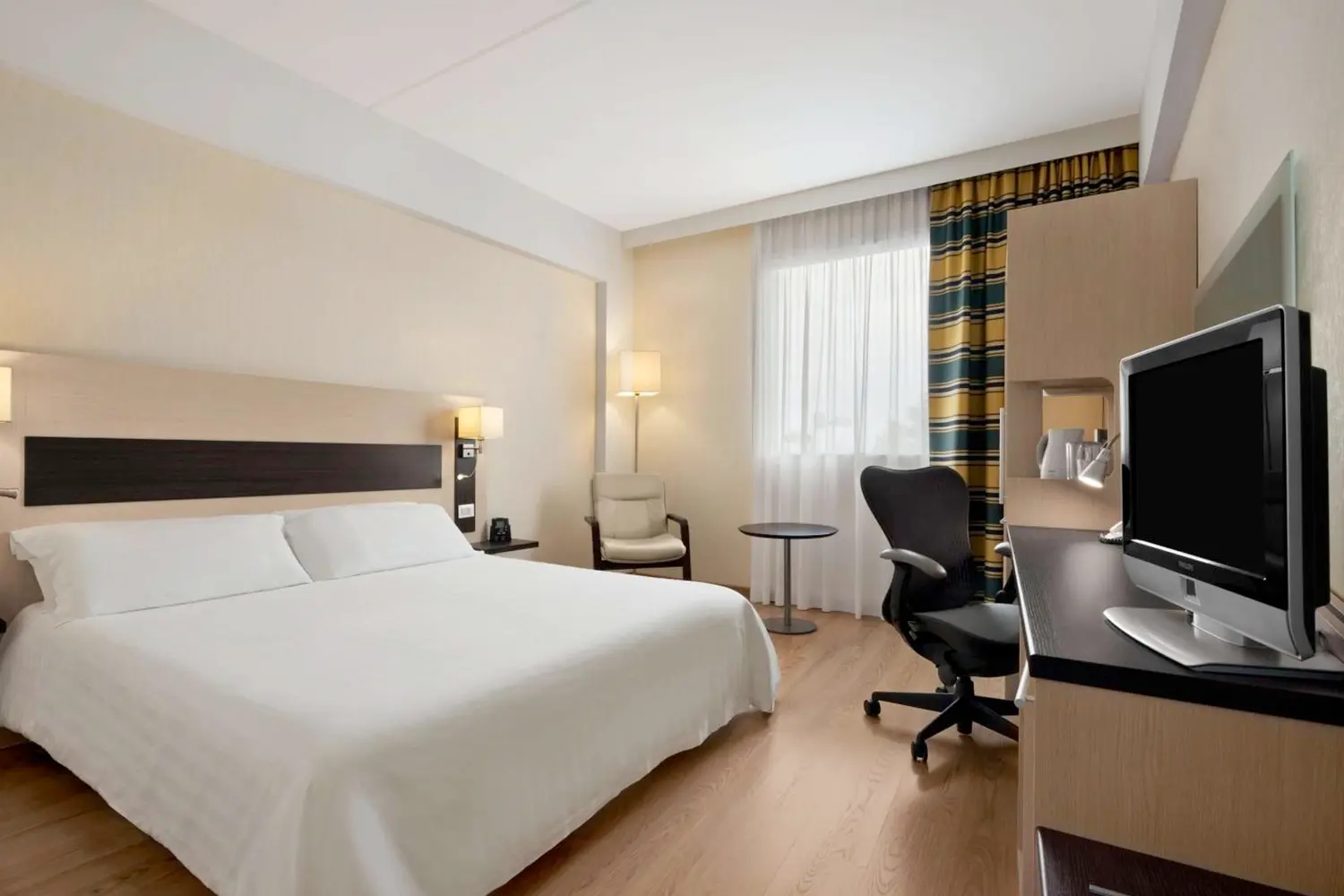 A room with a bed, desk, and chairs at Hilton Garden Inn Rome Airport