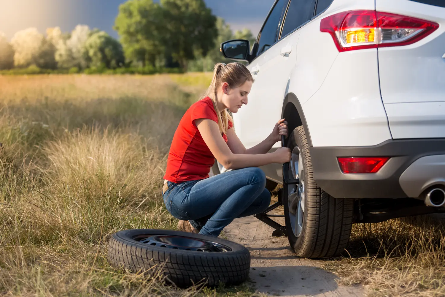 Young woman using jack to lift her car with flat tire and unscrew wheel nuts