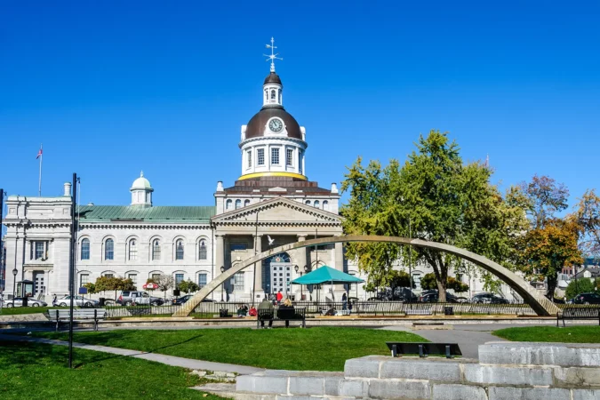 Tourists sit on a bench in front of city Hall of Kingston and Confederation arch fountain, Ontario Canada