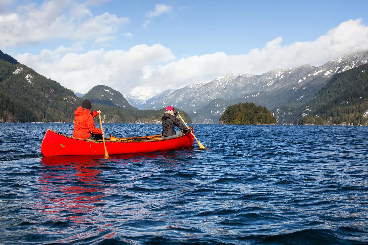 Couple friends on a wooden canoe are paddling in an inlet surrounded by Canadian mountains. Taken in Indian Arm, near Deep Cove, North Vancouver, British Columbia, Canada.