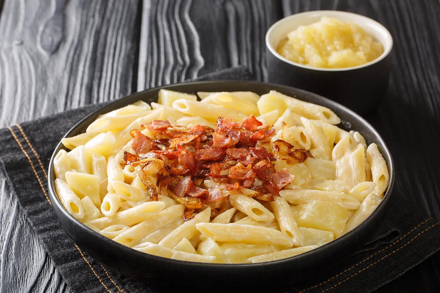 Authentic Swiss Alplermagronen - pasta with potatoes and cheese and fried onions, bacon close-up in a plate on the table.