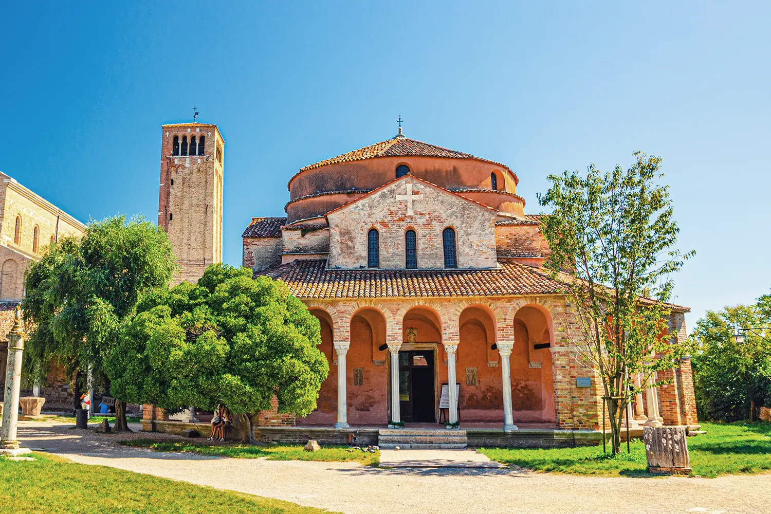Church of Santa Fosca building on Torcello island, Cathedral of Santa Maria Assunta with bell tower campanile, blue clear sky background. Venetian Lagoon, Veneto Region, Northern Italy.